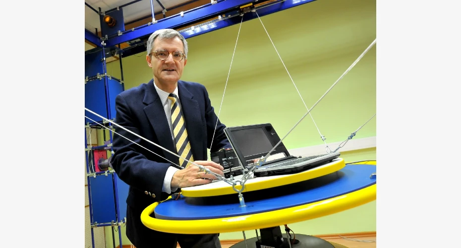 Photo of Andrzej Bartoszewicz stood by a blue and yellow round table, with a laptop and equipment nearby