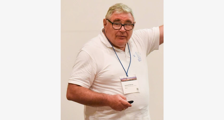 Photo of Leonid Fridman stood in front of and pointing at a whiteboard during a talk